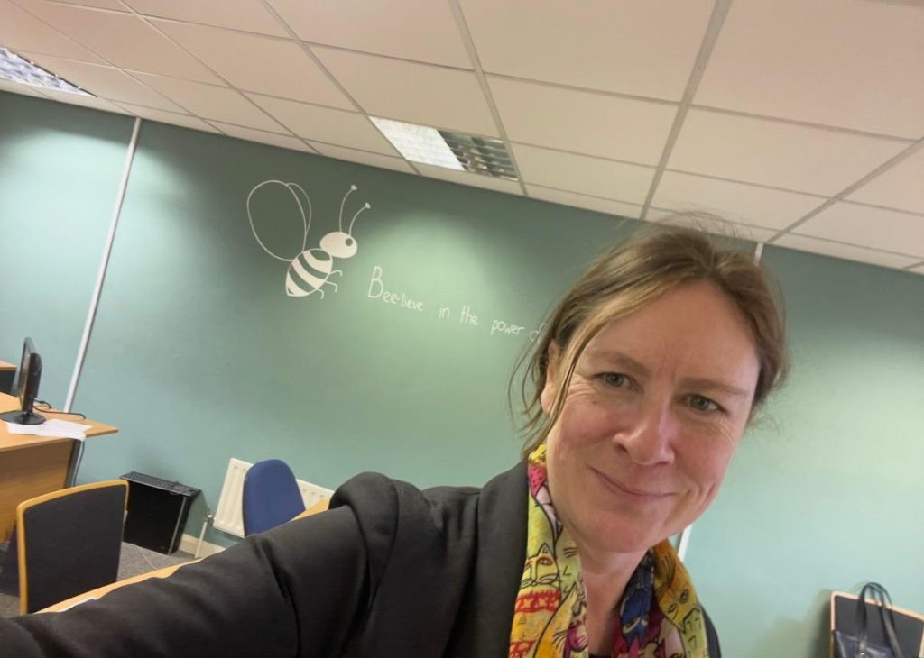 Tracey in the office with typically messy hair and the Arctic Bee logo behind her